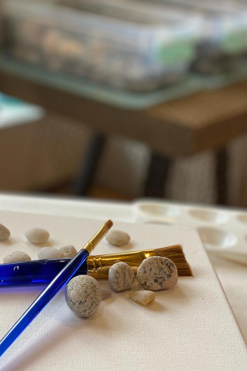 Decorative items including stones, a blue paint brush on a canvas surface with a blurred background.